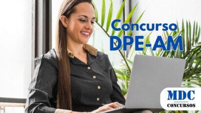 Mulher de cabelos longos e castanhos, vestindo camisa preta com detalhes bege, sorrindo enquanto usa um laptop prateado. Ela está sentada em uma cadeira confortável, cercada por plantas verdes, perto de uma janela com luz natural - DPE AM abre Concurso com remuneração de R$ 19.134