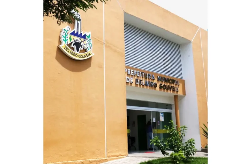 Fachada da Prefeitura Municipal de Delmiro Gouveia com parede amarela, brasão do município na lateral, entrada principal com portas de vidro e identificação institucional acima. Foto: Divulgação/Prefeitura de Delmiro Gouveia-AL