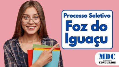 Jovem mulher de cabelos castanhos longos, sorridente, usando óculos redondos e camisa xadrez azul. Ela segura pastas coloridas nos braços e aponta com o dedo indicador para a direita. O fundo é rosa sólido - Educação de Foz do Iguaçu abre 200 Vagas para Professor em Processo Seletivo