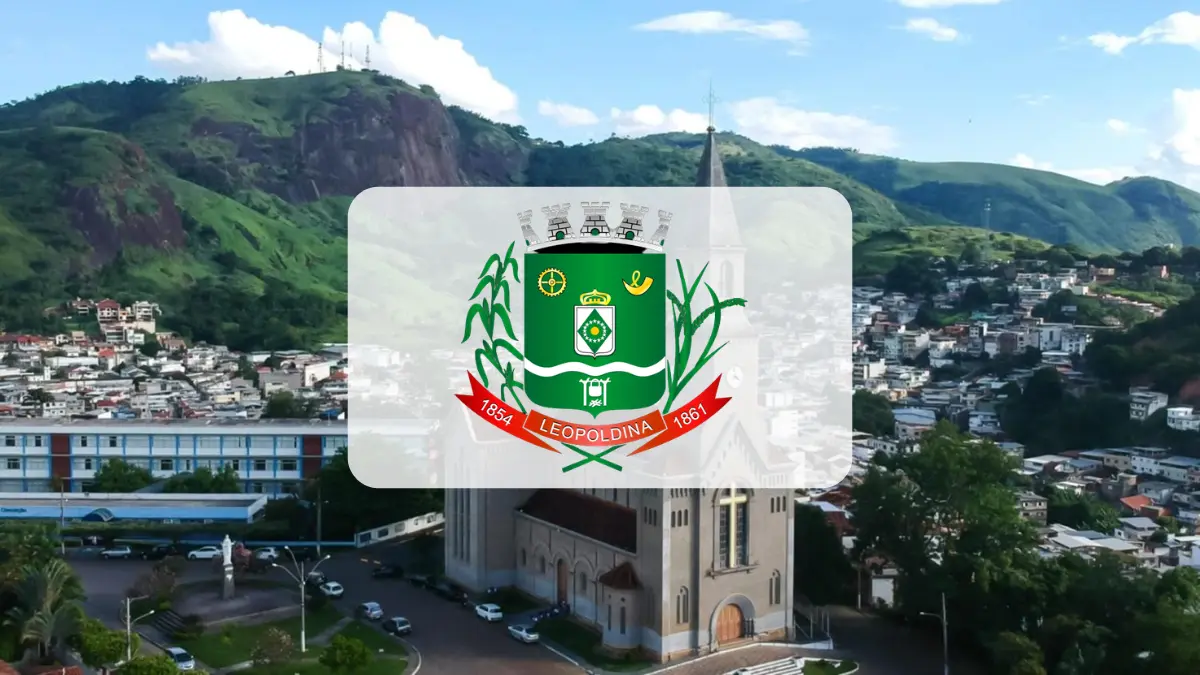 Leopoldina/MG abre processo seletivo com salários de R$ 3.905,25 1 Vista aérea da cidade de Leopoldina, em Minas Gerais, com destaque para o brasão oficial do município centralizado sobre a imagem de uma catedral e montanhas ao fundo. Foto: Divulgação/Câmara Municipal de Leopoldina-MG (João Gabriel Baía Meneghite)