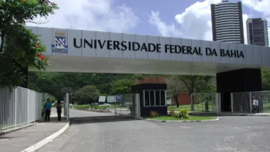 Portal de entrada do campus da UFBA, com letreiro branco escrito Universidade Federal da Bahia sobre pórtico de concreto, guarita, árvores e prédio ao fundo, instituição que oferece especialização EaD gratuita
