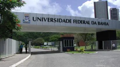 Portal de entrada do campus da UFBA, com letreiro branco escrito Universidade Federal da Bahia sobre pórtico de concreto, guarita, árvores e prédio ao fundo, instituição que oferece especialização EaD gratuita