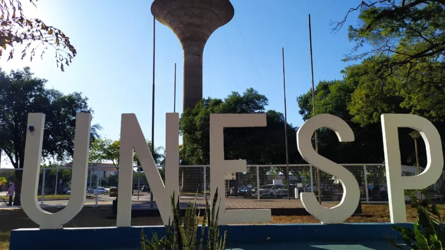 Letras brancas em três dimensões formando a sigla UNESP ao ar livre, com caixa d'água e árvores ao fundo, ilustrando a especialização EaD gratuita Unesp