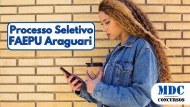 Processos Seletivos 2 Uma mulher jovem de perfil, com longos cabelos cacheados em tons de castanho e loiro, veste uma jaqueta jeans azul e segura um celular na mão esquerda enquanto apoia um copo reutilizável com tampa preta na mão direita, contra uma parede de tijolos amarelos - FAEPU Araguari (MG) oferece salários de Até R$ 5.765 em Processo Seletivo