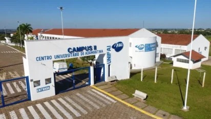 Fachada do Centro Universitário de Adamantina (FAI) com portão de entrada, letreiros azuis identificando o Campus II e prédios brancos de telhado cerâmico sob céu azul.