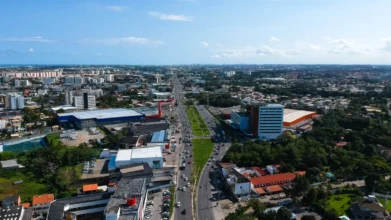 Vista aérea de Lauro de Freitas mostrando avenida central movimentada, prédios comerciais e residenciais ao redor e áreas verdes distribuídas pela cidade. Foto: Divulgação/Prefeitura de Lauro de Freitas-BA