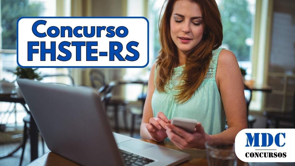 FHSTE RS oferece 21 vagas e salários de até R$ 6.259 em Concurso 1 Mulher de cabelos ruivos e vestido verde-água sentada em um café, segurando um smartphone enquanto olha para a tela. Na mesa há um laptop aberto, uma xícara e um copo com água. O ambiente é iluminado, com grandes janelas ao fundo mostrando árvores e carros estacionados - FHSTE RS oferece 21 vagas e salários de até R$ 6.259 em Concurso