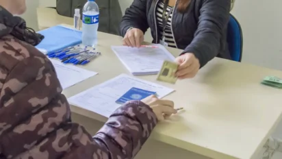 Pessoa entrega documento de identificação em balcão com papéis, carteira de trabalho e canetas sobre a mesa. Foto: Divulgação/Prefeitura de Curitiba/PR