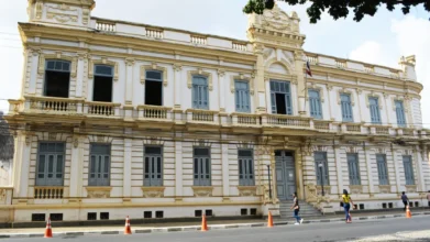 Fachada de prédio histórico, Sede da Prefeitura de Feira de Santana na Bahia, de estilo neoclássico, com janelas altas, detalhes ornamentais, pedestres na calçada e cones de trânsito na via em frente. Foto: Divulgação/Prefeitura de Feira de Santana-BA