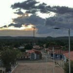 Vista aérea de Francisco Ayres-PI ao entardecer, com casas de telhado vermelho, torres de comunicação e vegetação ao fundo.