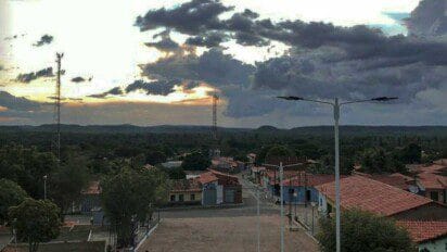 Vista aérea de Francisco Ayres-PI ao entardecer, com casas de telhado vermelho, torres de comunicação e vegetação ao fundo.
