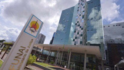 Prédio moderno da sede da FUNAI em Brasília com fachada espelhada e placa institucional em destaque no primeiro plano.