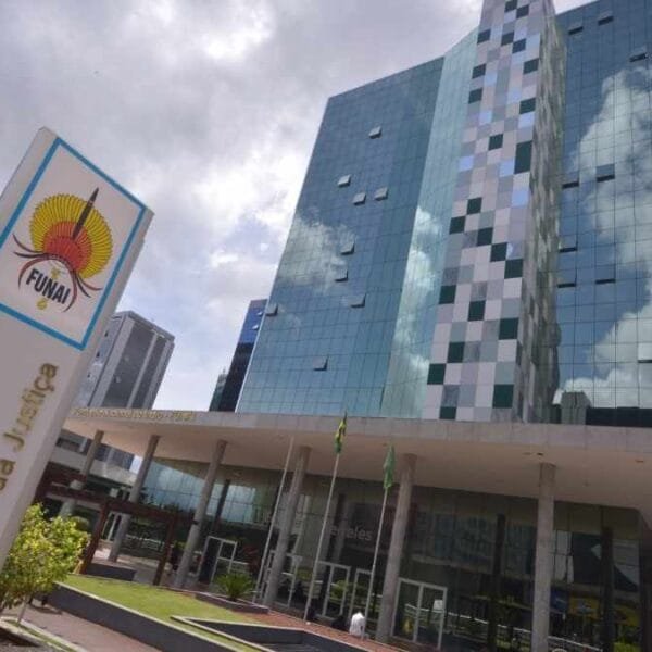 Prédio moderno da sede da FUNAI em Brasília com fachada espelhada e placa institucional em destaque no primeiro plano.