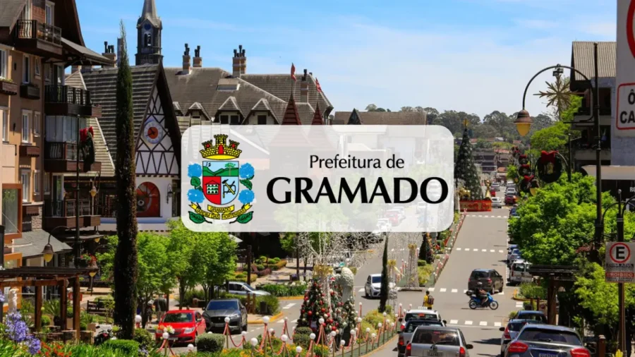 Vista panorâmica de uma rua em Gramado com arquitetura típica europeia, decoração natalina, carros em movimento e o logotipo da Prefeitura de Gramado ao centro. (GRAMATUR)