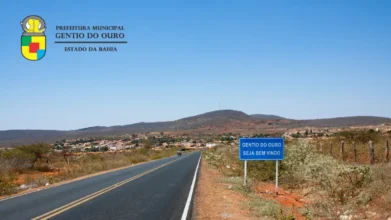 Gentio do Ouro/BA lança concurso com 46 vagas e salários de até R$ 3,9 mil 2 Rodovia de acesso a Gentio do Ouro, na Bahia, com placa de boas-vindas à cidade, área urbana ao fundo e paisagem típica do sertão sob céu azul. Foto: Divulgação/Prefeitura de Gentio do Ouro-BA