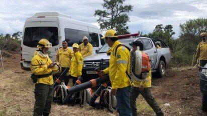 Brigadistas do ICMBio em campo, usando uniformes amarelos e equipamentos de combate a incêndios, com veículos ao fundo.