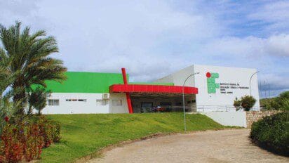 Fachada do campus Jacobina do Instituto Federal da Bahia (IFBA), com estrutura branca, detalhes em vermelho e verde, e logo da instituição na parede.