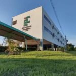 Imagem mostra prédio do IFPA com fachada branca, logotipo em destaque, dois andares, área aberta com pilares, cobertura para pedestres e paisagismo bem cuidado.