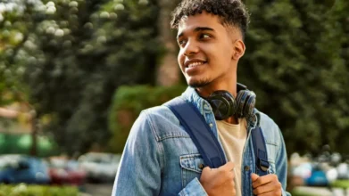 Jovem sorridente com mochila e fones de ouvido no pescoço em ambiente externo arborizado. Foto: krakenimages.com/Freepik