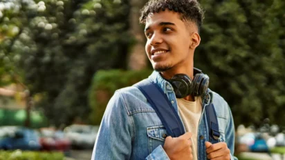Jovem sorridente com mochila e fones de ouvido no pescoço em ambiente externo arborizado. Foto: krakenimages.com/Freepik