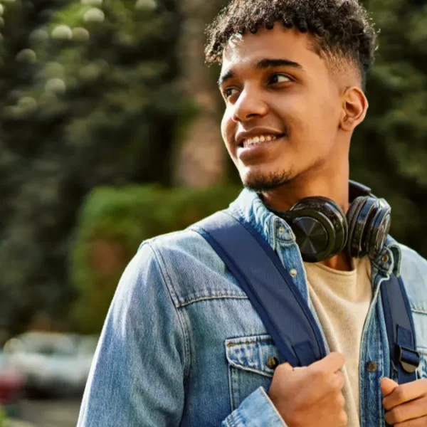 Jovem sorridente com mochila e fones de ouvido no pescoço em ambiente externo arborizado. Foto: krakenimages.com/Freepik