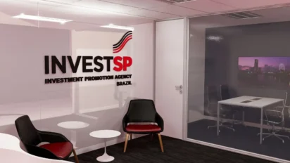 Interior de um escritório moderno com o logotipo da IINVESTSP em uma divisória de vidro, poltronas de espera e uma sala de reuniões ao fundo.