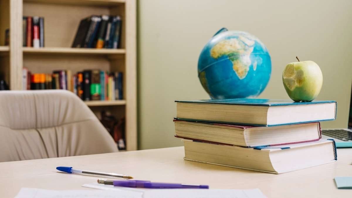 Ilha Grande PI abre seleção com 14 Vagas de até R$ 2.433,88 1 Imagem de uma mesa de estudo ou trabalho com três livros empilhados, um globo terrestre e uma maçã verde parcialmente comida sobre os livros. Em primeiro plano, há duas canetas e folhas de papel, sugerindo um ambiente acadêmico. Ao fundo, uma estante com livros variados e uma cadeira de escritório completam a cena, remetendo a um espaço educacional ou de leitura. (Ilha Grande PI)