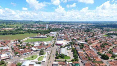 Processos Seletivos 3 Imagem aérea da cidade de Inhumas-GO, com áreas urbanas, residências, estádio de futebol e vegetação ao fundo em um dia de céu azul com nuvens