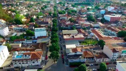 Vista aérea da cidade de Ipanema/MG, com ruas arborizadas, prédios baixos e casas distribuídas de forma organizada.