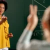 Professora em sala de aula aponta para aluna que levanta a mão, com equações matemáticas escritas no quadro. Foto: Drazen Zigic/Freepik