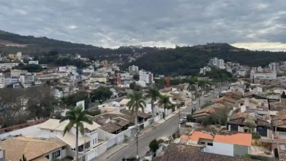 Vista panorâmica de Itabira em Minas Gerais com casas, prédios, ruas arborizadas e morros ao fundo sob céu nublado. Foto: HVL/Wikipédia