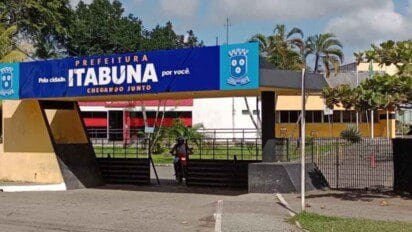 Entrada da Prefeitura de Itabuna com estrutura azul e amarela, contendo o brasão do município e os slogans “Pela cidade por você” e “Chegando junto”.