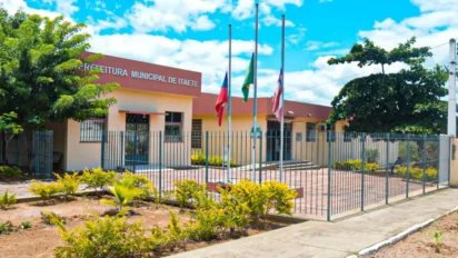 Fachada da Prefeitura Municipal de Itaetê com jardim, grades frontais, três mastros com bandeiras e céu azul ao fundo. Foto: Divulgação/Prefeitura de Itaetê-BA