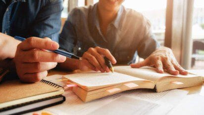 Duas pessoas estudando juntas com livros, cadernos e anotações sobre a mesa.