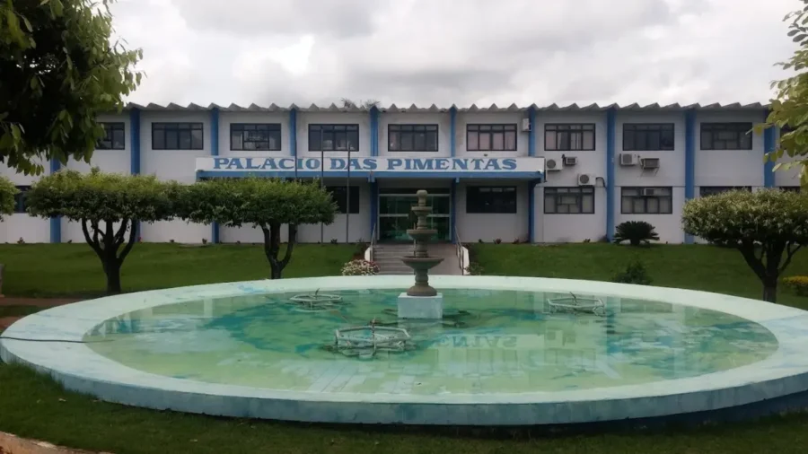 Fachada do Palácio das Pimentas (Sede da Prevfeitura de Itarumã-GO), um prédio branco e azul de dois andares com gramado e uma fonte circular em primeiro plano.