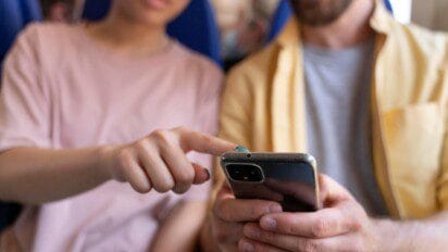 Duas pessoas sentadas, uma apontando para a tela de um smartphone que a outra segura com as duas mãos. Foto: Freepik