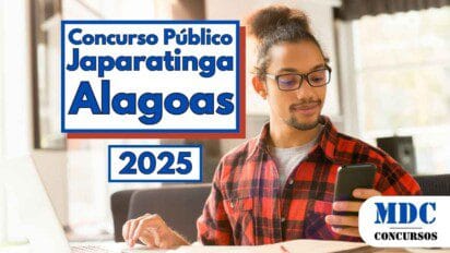 Homem jovem de cabelos presos em coque e usando óculos, veste camisa xadrez vermelha e cinza e está sentado em frente a um notebook enquanto segura um celular e sorri levemente, ao fundo há uma janela com luz natural entrando no ambiente; à esquerda da imagem há um banner com os dizeres Concurso Público Japaratinga Alagoas 2025 e no canto inferior direito está o logotipo da MDC Concursos
