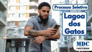 Processos Seletivos 3 Homem de barba e cabelos cacheados, usando camisa polo cinza e fones de ouvido no pescoço, apoia-se em um patinete elétrico enquanto olha para o celular em um ambiente urbano com prédios modernos ao fundo - Lagoa dos Gatos (PE) Abre Vagas com Salário de R$ 2.824 para ACS em Processo Seletivo