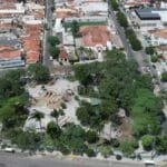 Vista aérea do centro de Limoeiro-PE, destacando uma praça arborizada cercada por ruas, casas e comércios.