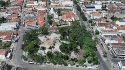 Vista aérea do centro de Limoeiro-PE, destacando uma praça arborizada cercada por ruas, casas e comércios.