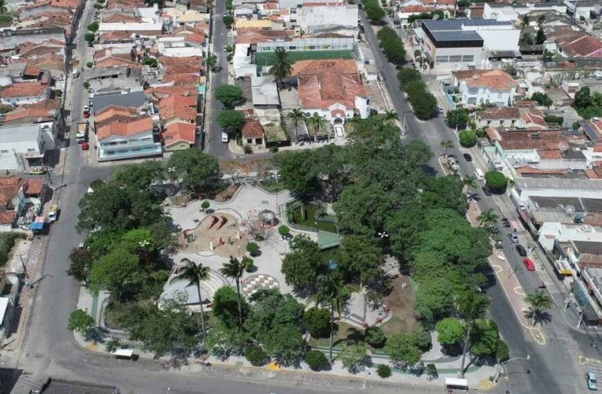 Vista aérea do centro de Limoeiro-PE, destacando uma praça arborizada cercada por ruas, casas e comércios.