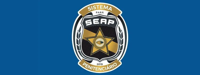 Brasão da SEAP Pará com uma estrela dourada ao centro, contendo um olho estilizado, cercada por ramos e os dizeres "Sistema Penitenciário Pará SEAP 2019" em fundo azul.