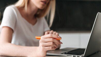 Processos Seletivos 8 Mulher segurando uma caneta laranja enquanto utiliza um notebook.