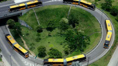 Ônibus articulados amarelos da MOBI Rio circulando em uma rotatória cercada por área verde.