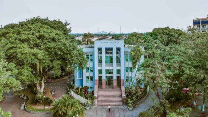 Fachada do Palácio Anchieta, sede da Prefeitura de Magé, com escadaria central, prédio azul e rodeado por árvores e jardins.