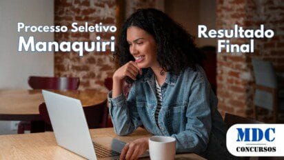 Mulher jovem de cabelos cacheados e pele morena usa um laptop em um café aconchegante com parede de tijolos aparentes, sorrindo enquanto olha para a tela. Ela veste uma jaqueta jeans sobre uma blusa listrada e tem uma xícara branca ao lado - Manaquiri (AM) divulga Resultado Final de Processo Seletivo