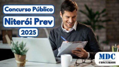Homem sorridente, vestindo camisa branca e suéter cinza escuro, sentado à mesa com um laptop aberto, segura uma prancheta e uma caneta enquanto parece revisar anotações; no canto inferior direito há o logotipo da empresa MDC Concursos e no canto superior esquerdo está escrito "Concurso Público Niterói Prev 2025" em letras azuis com moldura branca e azul em destaque sobre um fundo de escritório moderno com planta decorativa e iluminação suave