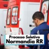 A imagem mostra várias ambulâncias do SAMU 192 enfileiradas, com destaque para a traseira dos veículos nas cores branca e vermelha. Em primeiro plano, um profissional de saúde com uniforme azul escuro e o logotipo do SAMU nas costas aparece de perfil, aparentemente conferindo informações em um documento. Na parte inferior da imagem, há uma faixa com os dizeres “Processo Seletivo Normandia RR”, indicando a divulgação de uma seleção pública.