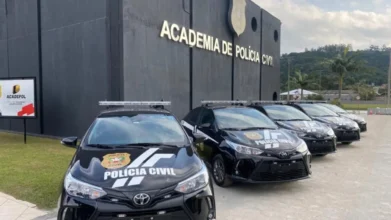 PCSC abre concurso com 300 vagas e salários de até R$ 10.270,00 2 Viaturas da Polícia Civil de Santa Catarina estacionadas em frente ao prédio da Academia de Polícia Civil, com fachada escura e identificação institucional. Foto: Divulgação/PCSC