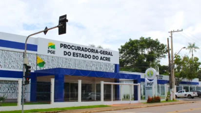 Fachada da Procuradoria-Geral do Estado do Acre com prédio moderno em azul e branco, exibindo o letreiro oficial do órgão e bandeiras posicionadas na entrada. Foto: Divulgação/PGE-AC